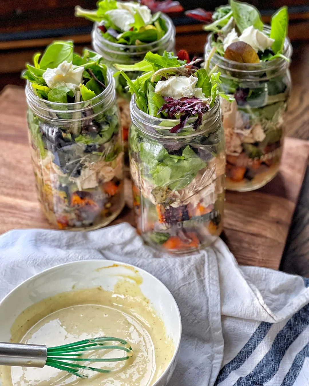 Cuatro frascos con ensalada y un bowl de aderezo casero